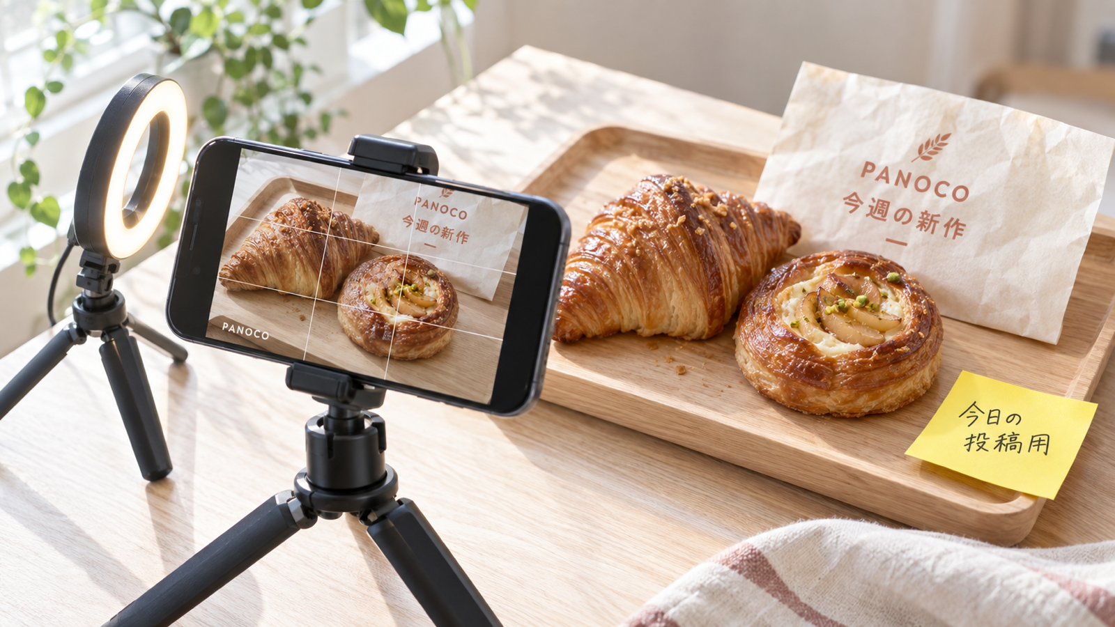スマートフォンを置いたスタンドと、投稿の予定を書き込んだ紙のカレンダーが並ぶデスク