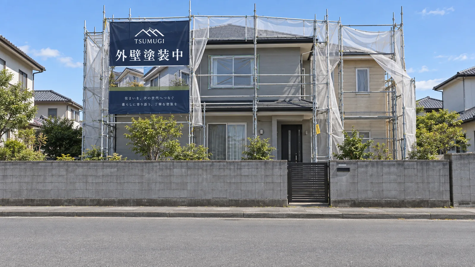 外壁の塗り替え工事中の2階建ての家。足場の間から塗り直した外壁の色が見え、足場には施工会社の工事案内の看板が掛かっている